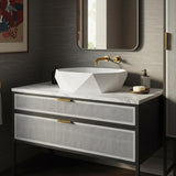 A geometric Carrara marble vessel sink resting on a rattan-front vanity with brass hardware in a luxury bathroom.