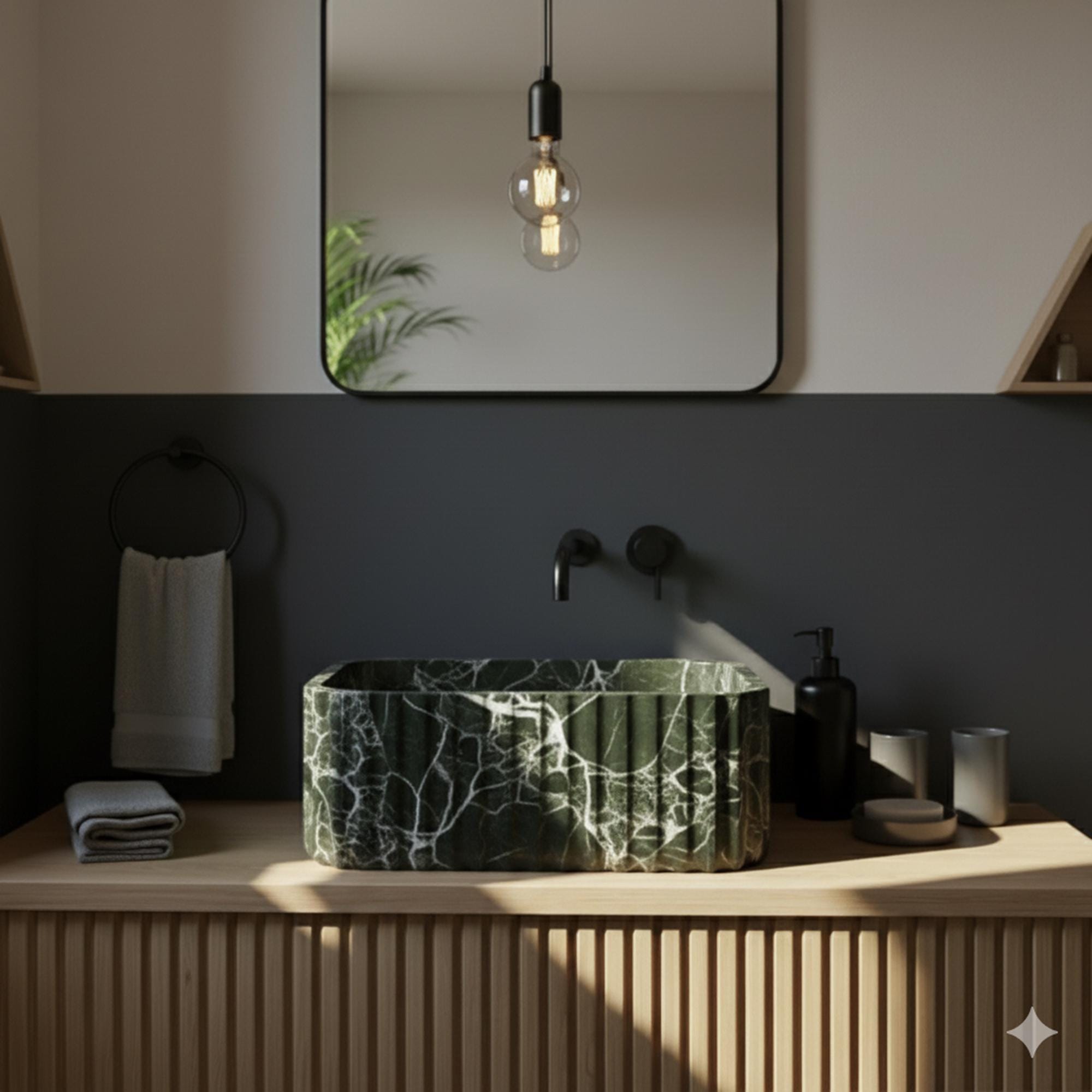 Elegant dark green marble bathroom sink with striking veining, hand-carved and set on modern oak vanity in a moody interior