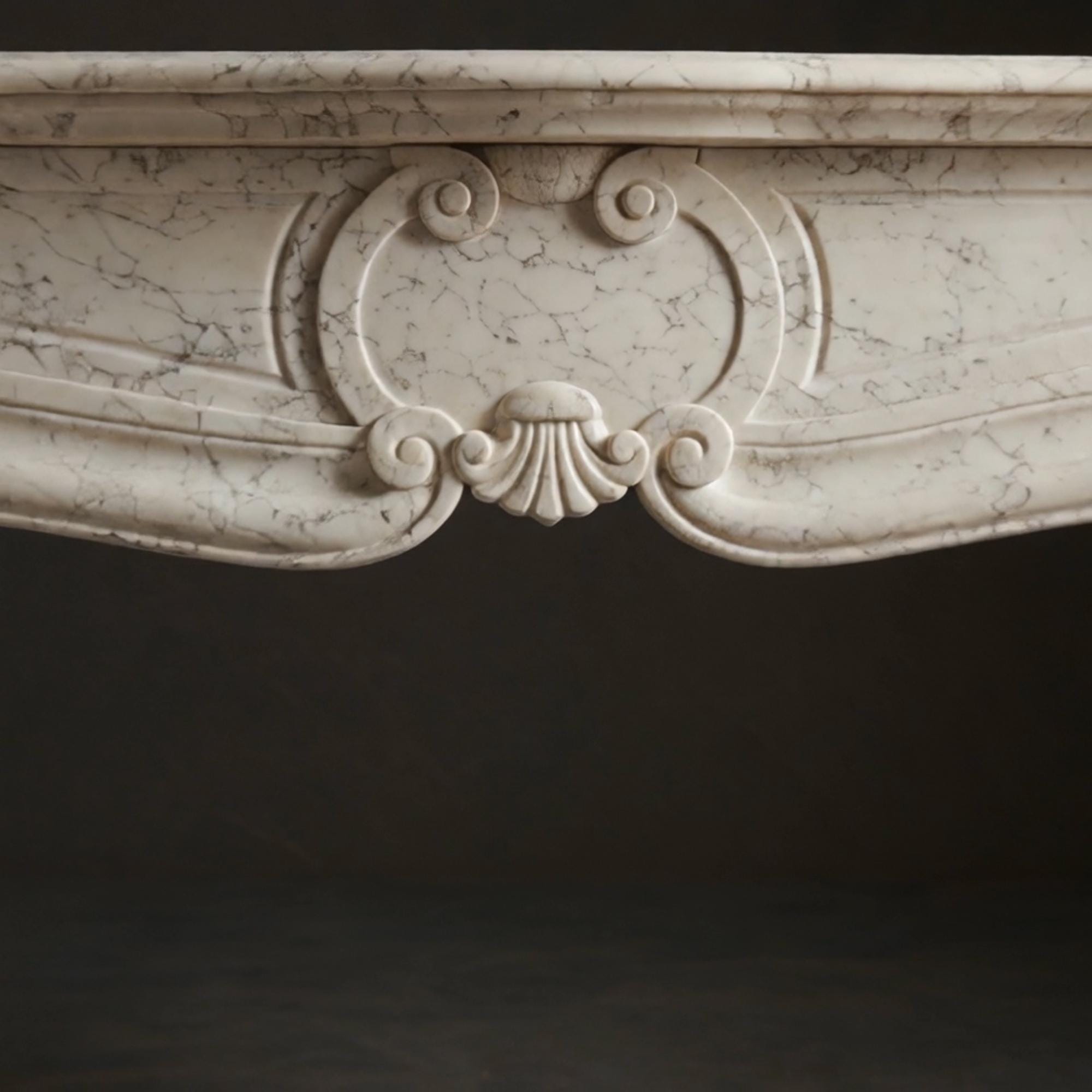 Hand-carved cream marble mantel featuring elegant curves, decorative scrolls, and central shell detail