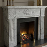 Traditional white Carrara marble fireplace mantel with hand-carved shell and fluted detailing around a black firebox